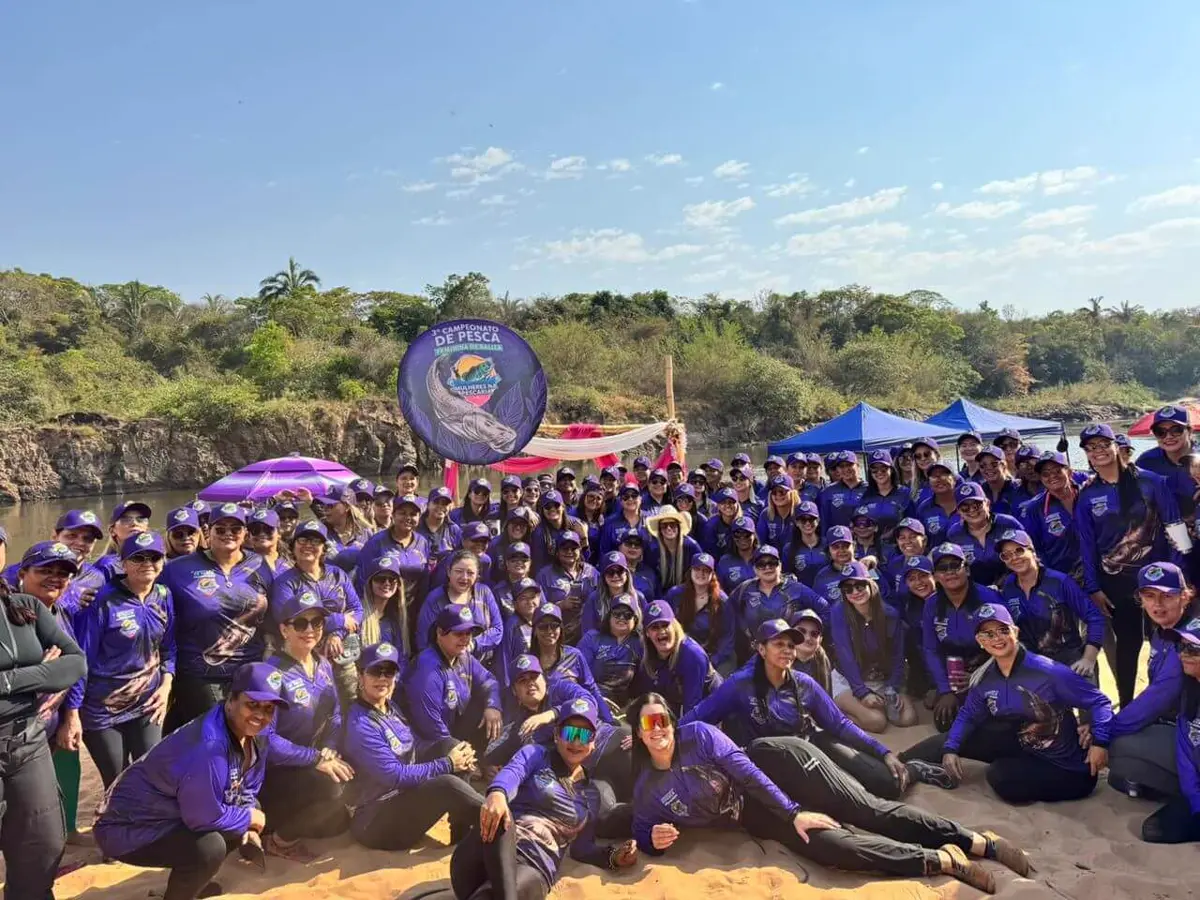 Participantes de campeonato feminino de pesca com camisetas roxas personalizadas na beira do rio