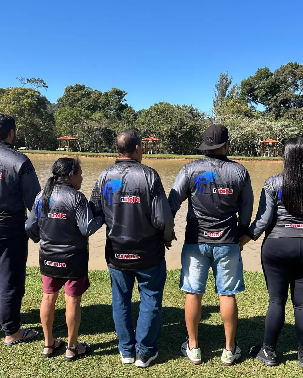 Família de costas mostrando os nomes personalizados nas camisetas, em frente a um lago